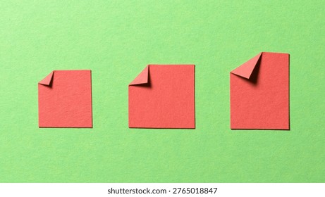 Red blank paper message notes or sheets with folded edge dog-ear earmark and copy space for text on green background, top view flat lay conceptual desk backdrop