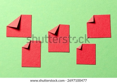 Red blank paper message notes or sheets with folded edge dog-ear earmark and copy space for text on green background, top view flat lay conceptual desk backdrop