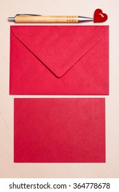 Red blank sheet of paper with envelope and little heart, pen on wooden surface. Background for valentines day or wedding card.