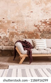 Red Blanket And Cushions On Grey Settee In Living Room Interior With Brick Wall And Carpet. Real Photo