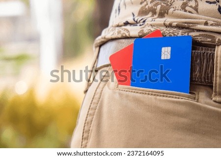 Red and blue bank cards are in the pocket of light-colored trousers. The man has bank cards in his pocket.