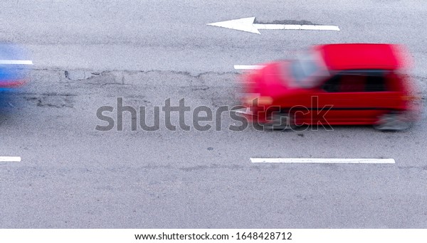 Red and blue car fast moving on asphalt road in\
the city. Blurred motion of fast speed compact car on asphalt road.\
Urban transport with rush hour concept. Travel by car. Car fuel\
consumption concept.