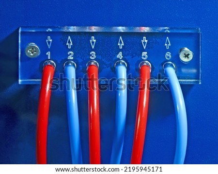 red and blue connected cables pack heap on blue transparent plexiglass control panel surface fixed with few screw closeup. color power electricity numbers concept