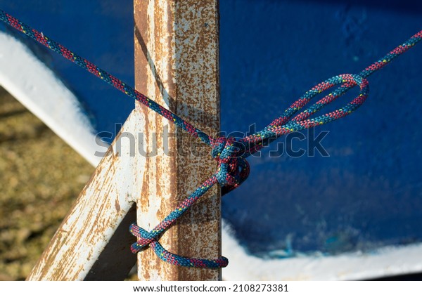 A red and blue mooring line is tied to the steel\
frame of the trestle on which a pleasure craft is moored during\
winter storage.