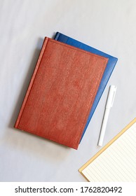 Red And Blue Notebooks With A White Pen On A Gray Cloth Surface. Keeping Journals And Diaries. Notebook Designer And Writers. Recordkeeping. Meeting Minutes On The Desktop