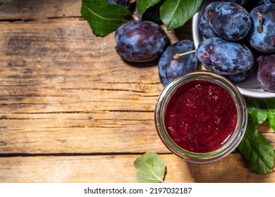 Red blue plum jam in small jar. Homemade autumn plum jam with fresh fruits. Fall preparations and canning on wooden table background copy space