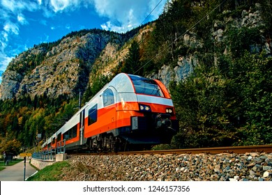 Red Blue Train In Motion In Austrian Alps Mountains. High Speed Mountain Train Arrives At Hallstatt Obertraun Train Station In Mountains. Location: Resort Village Hallstatt, Salzkammergut, Austria.