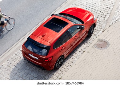 Red BMW M135i parked on the street. The cyclist passes the car. Top view. Model F40, produced from 2019. 306 HP engine, acceleration 0-100 km-h: 4.8 s - Katowice, Poland- 09.16.2020