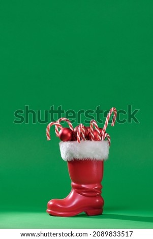 Red boot of Santa Claus with a white fur. Christmas boot stocking with gifts on a green background. Red Santa's boot with copyspace. Happy Christmas. Santa Claus boot stuffed with presents