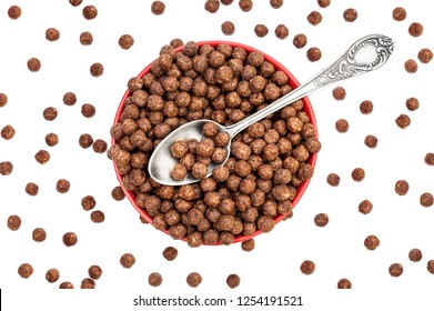 Red bowl with chocolate corn balls and spoon on white. Top view.