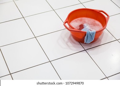 Red Bowl Filled With Detergent Or Soap And Water With Cloth Standing On Tiled Floor