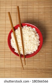 Red Bowl Of Rice With Wooden Chopsticks And A Wood Place Mat 