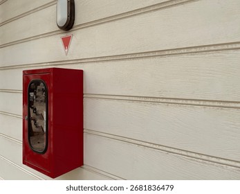 A red box containing a light fire extinguisher is mounted on a horizontal striped panel wall, with a round lamp decorating the home's walls.