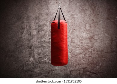 Red boxing bag hanging against gray rusty wall