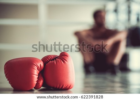 Red boxing gloves in the foreground, boxer is sitting on the boxing ring in the background