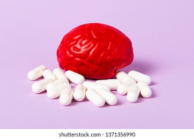 Rotes Gehirn auf rosafarbenem Hintergrund mit weißen Tabletten. Einige Tabletten für das Gehirn. Symbolisch für Drogen, Psychopharmaka, Nootropie und andere Arzneimittel. Das Medikament. Hirnbehandlung