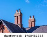 Red brick chimeys on a grey slate roof with a blue sky background on a sunny day
