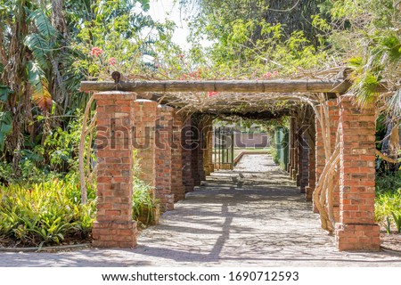 Red brick collumn alley-way pergola entrance with romantic tropical plants on a bright summer day in Port Elizabeth in South Africa.