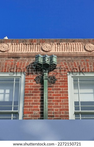 Red brick facade-AD1928 Victorian Gothic style building-fluted frieze-round flower motifs-rusty copper leader head and downpipe-The Corso pedestrian mall south side-Manly suburb. Sydney-NSW-Australia.