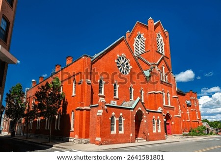 The red brick First United Methodist Church in Pittsfield, Massachusetts, United States, displays Gothic Revival arches, rose window and corner tower beneath a vivid summer sky.