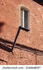 A Red Brick Old House With A White Window And A Metal Tube Coming Out Of The Wall. Low Angle Shot. Bright Sunny Day