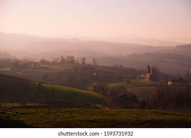 Red Brick Serb Orthodox Christian Church On Warm Winter Sunset In Surrounded With Grass Fields, Old Houses And Sheep In The Village Of Tutnjevac, Bosnia