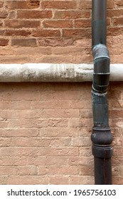 Red brick wall divided in the upper third by a horizontal line of marble and a longitudinal metal tube on the right
