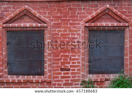 The red brick wall of old building with two windows shuttered partially by iron shutters with iron treillage. Moscow. Russia