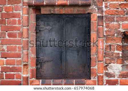The red brick wall of old building with window shuttered partially by iron shutters with iron treillage. Moscow. Russia