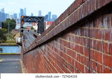 Red Brick Wall Of Rail Bridge Over Maribyrnong River With A Distance View Of Melbourne City