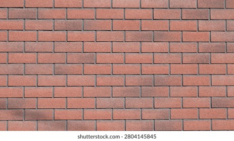 A red brick wall with smooth horizontal masonry. The surface of the blocks is rough and grainy. The shades range from terracotta to dark brown, with dark gray cement joints between the blocks.