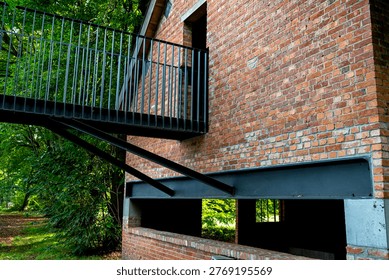 Red brick wall structure featuring a modern steel balcony in a green park