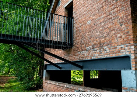 Red brick wall structure featuring a modern steel balcony in a green park