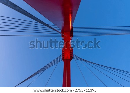 Red bridge pylon and cables creating an abstract pattern against a clear blue sky in Rotterdam, Netherlands