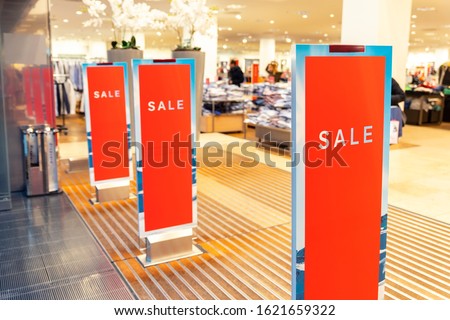Red bright sale banner on anti-thieft gate sensor at retail shopping mall entrance. Seasonal discount offer in store
