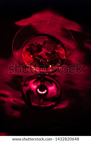 Red broken martini glass with red drink and red light on black background moody