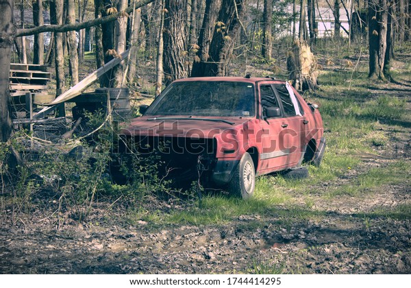 A red broken-down car next to brush and a stack a\
tires in a forest