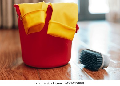 Red bucket, yellow gloves, broom, and dusting mop on hardwood floor - Powered by Shutterstock