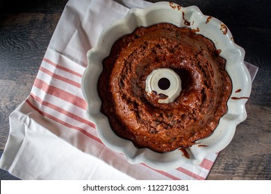 Red Bundt Pan With Baked Carrot Cake Inside Sitting On Red Striped Dish Towel On Farmhouse Table Top View