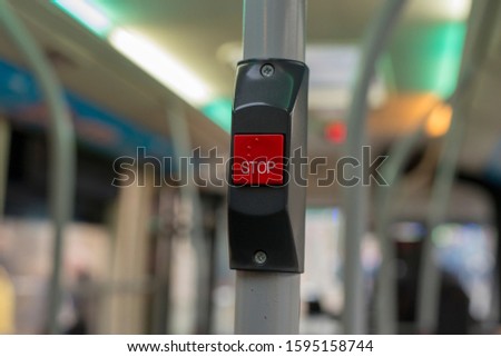 A red bus stop button on a bus which tells the driver to stop when a passenger presses it