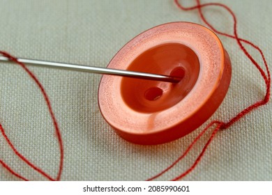 Red button with a needle with inserted thread on a white linen cloth close-up macro photography