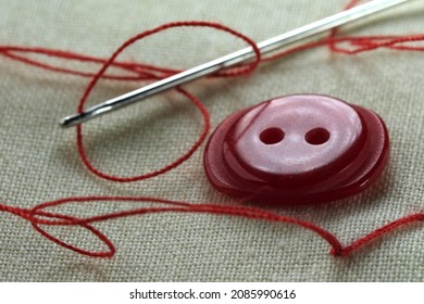 Red button with a needle with inserted thread on a white linen cloth close-up macro photography