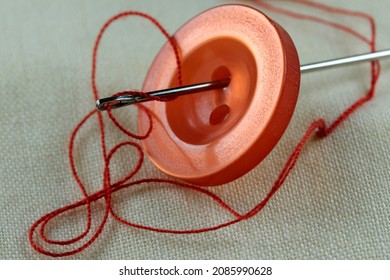 Red button with a needle with inserted thread on a white linen cloth close-up macro photography