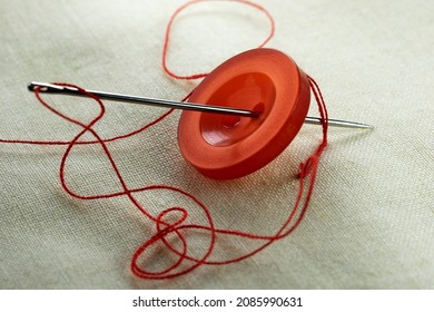 Red button with a needle with inserted thread on a white linen cloth close-up macro photography
