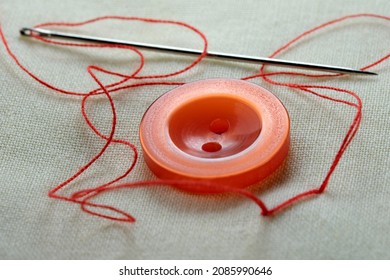 Red button with a needle with inserted thread on a white linen cloth close-up macro photography