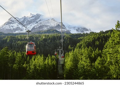 red cable car Surrounded by lush green pines, thick clouds, behind snow-capped mountains, Kriens, Switzerland.