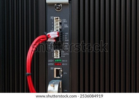 Red cable connecting to input output module of a programmable logic controller with visible leds and communication ports