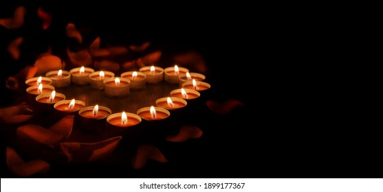 Red candles are arranged in the shape of a heart on a dark background. There are rose petals all around. Banner with space for text. - Shutterstock ID 1899177367