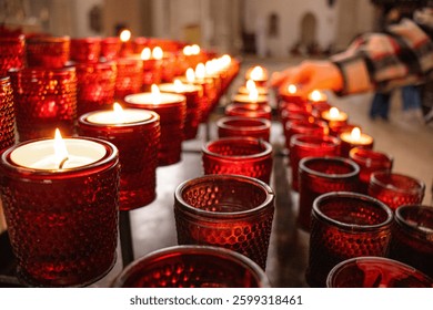 Velas rojas ardiendo en la iglesia, la mano es visible encendiendo una vela, simbolizando la oración, la esperanza y la memoria, el brillo cálido de la llama y la atmósfera de oración