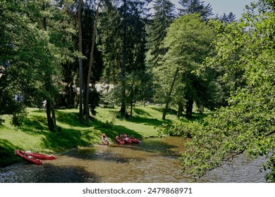 Red canoes are pulled up on the riverbank of a beautiful river flowing through a lush green forest - Powered by Shutterstock